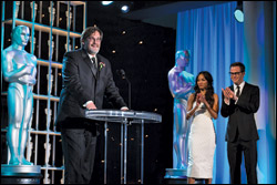 Richard Mall speaks at AMPAS’ Scientific and Technical Achievement Awards while presenters Zoe Saldana and Chris Pine look on.