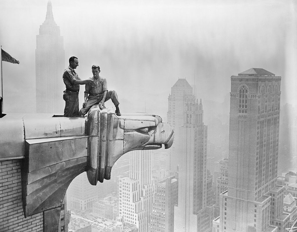 A man lights a fellow worker's cigarette as they take a break on a Chrysler Building gargoyle.