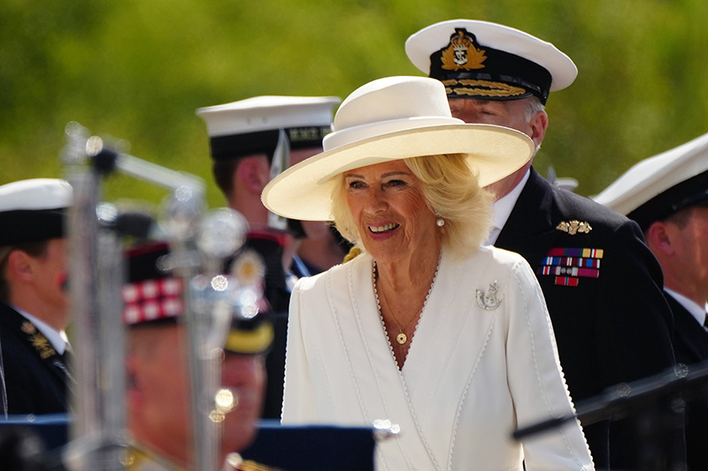 Queen Camilla wears white Dior dress and British bugle horn brooch for VJ Day celebration.