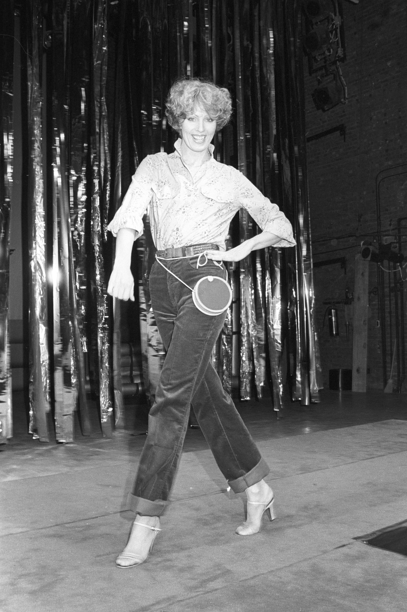 A model wears high-waisted and cuffed jeans with pumps, a circular chest-crossed bag and button down shirt..Article title: 'Gloria Vanderbilt: Making (air) waves